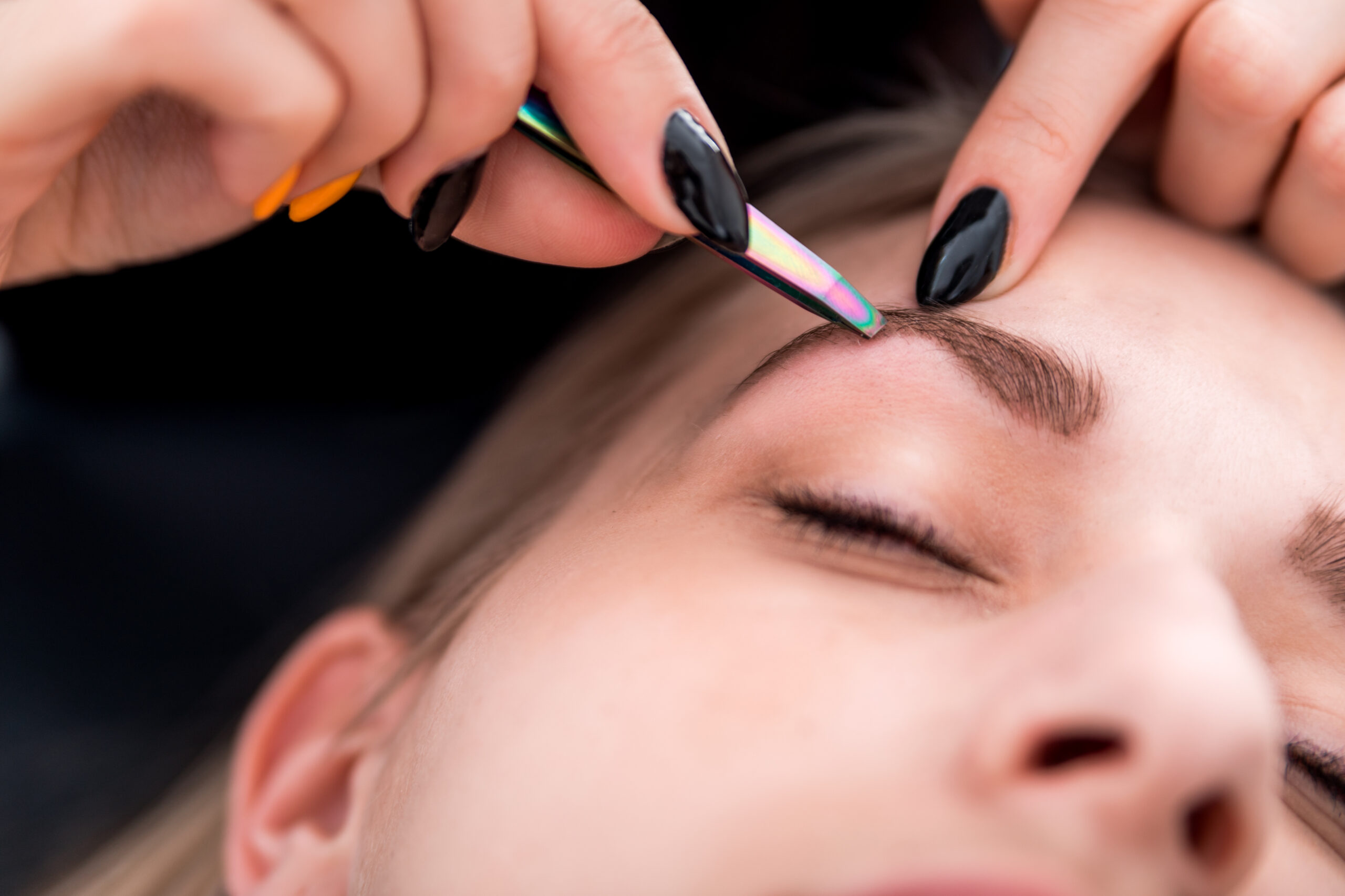 Esthéticienne épilant les sourcils d'une cliente avec une pince.